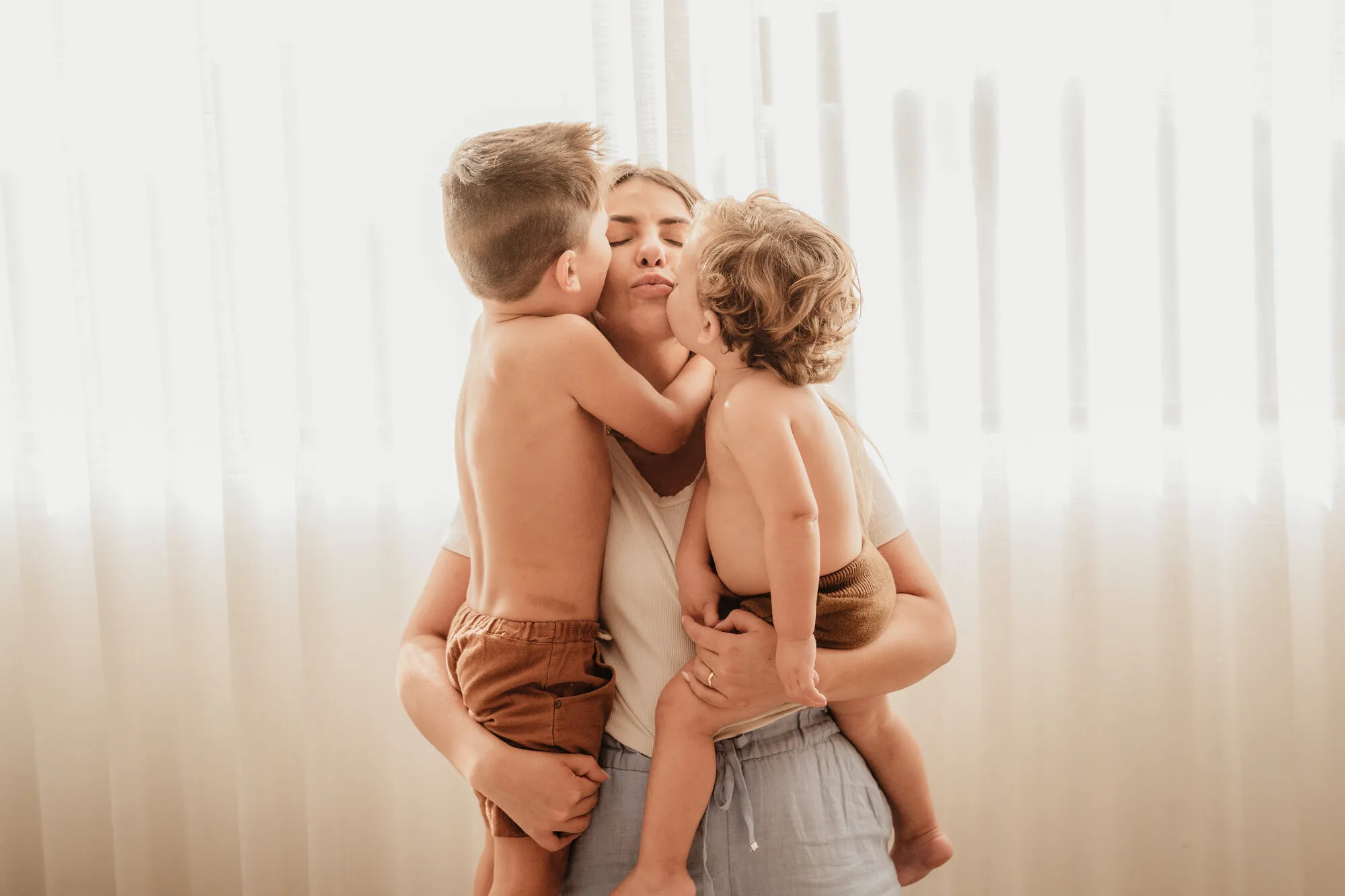 Mãe abraçando os dois filhos em contraluz durante ensaio de família no Estúdio Malice em Itu