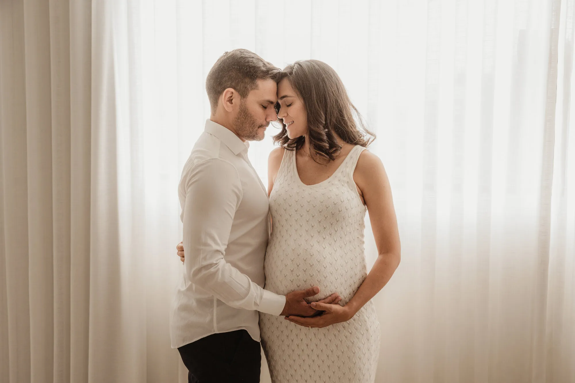Casal grávido em contraluz trocando carinho no ensaio gestante