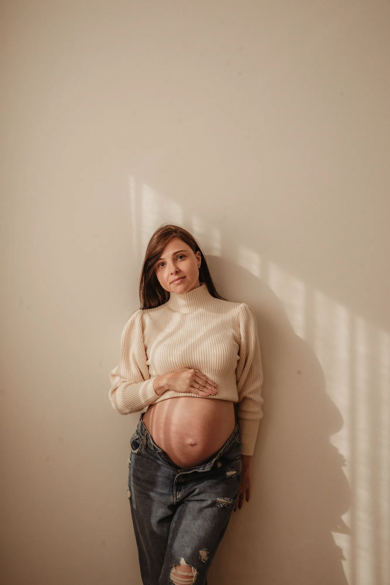Gestante segurando a barriga em ensaio de estúdio com luz suave