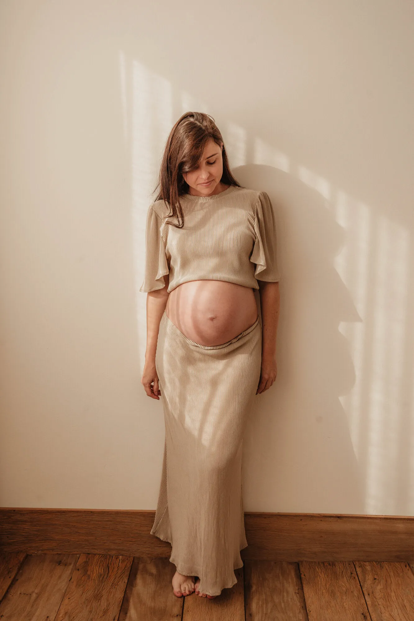 Gestante de vestido segurando a barriga em ensaio de estúdio