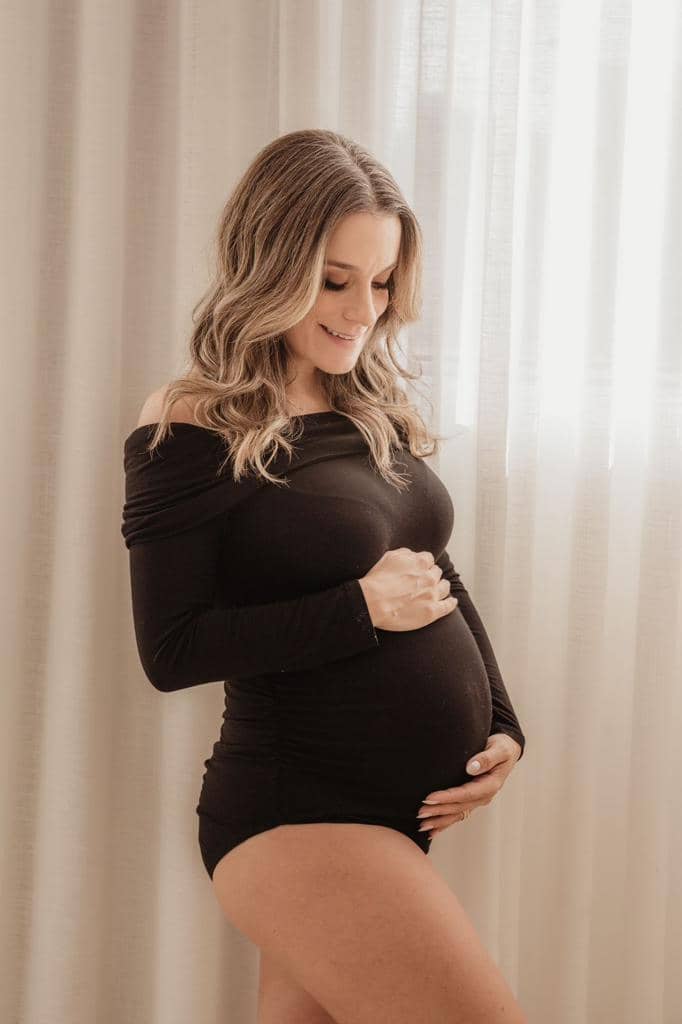 Gestante segurando a barriga com carinho em ensaio fotográfico