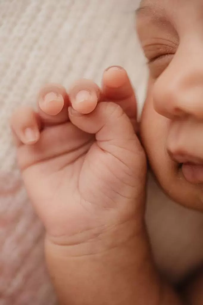 Recém-nascida enrolada em wrap com headband delicada, dormindo durante ensaio newborn